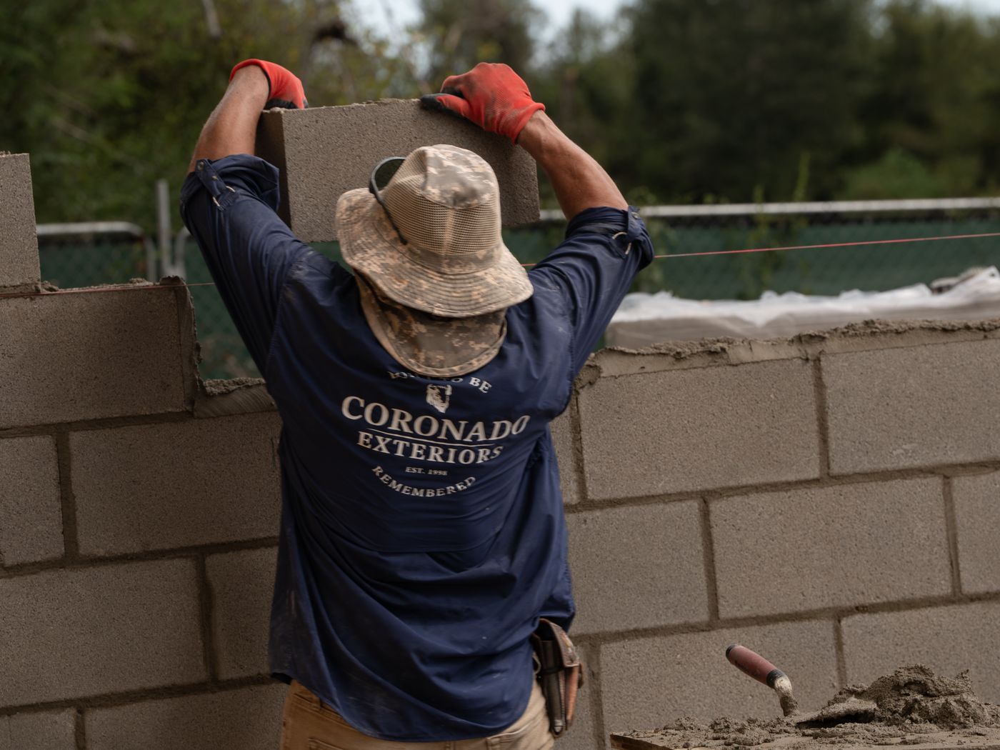 Mason lifting a concrete block onto a reinforced CMU wall in Houston